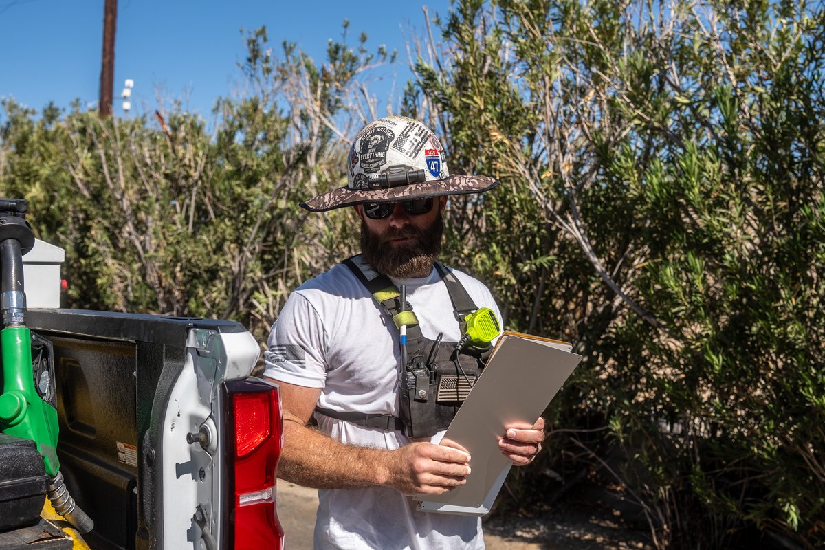 Lineman in a Half Hitch Woodland Camo sun shade reading a clipboard at the tailgate of his truck